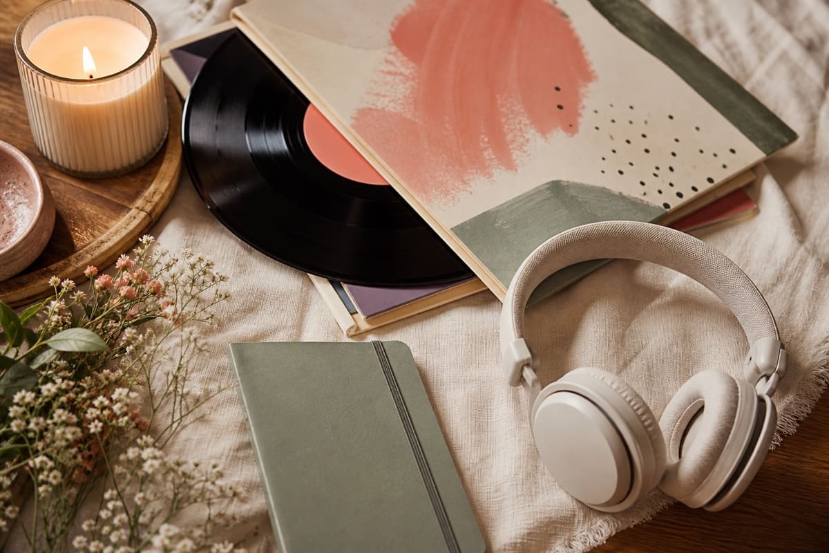 Vinyl records, modern headphones without logos, a small notebook, and warm candlelight arranged for a music lover for 16 of the Greatest Gifts to Get Your Music Loving Girlfriend on Christmas.