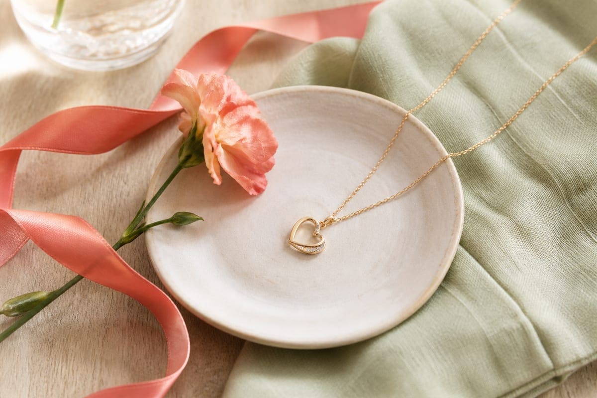 A necklace arranged on warm linen with a ceramic dish and a single flower stem for 15 Heart Necklaces Your Girlfriend Actually Wants!.